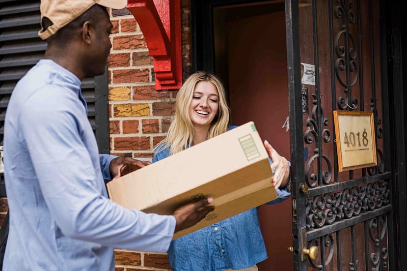 A woman is signing for her delivery with a courier, packaged in a green recyclable delivery box
