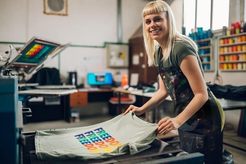 A woman is operating a machine for garment printing prints