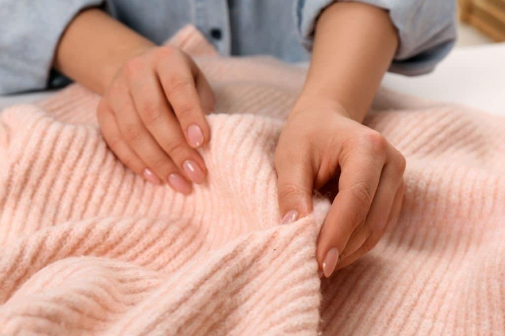 Woman touching soft pink knitted fabric
